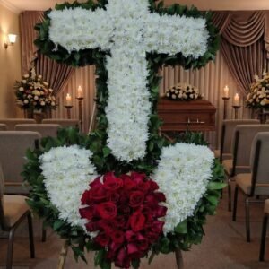 Corona fúnebre grande en forma de cruz blanca y corazón de rosas rojas en trípode, ubicada en sala de velación en Medellín